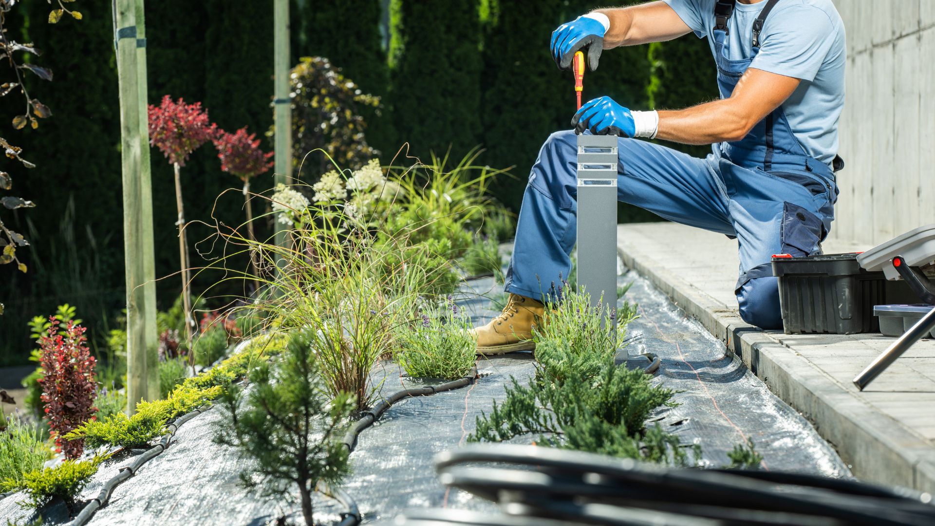 A man in blue overalls and gloves working on a garden